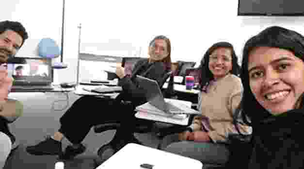 Two men and two women sat at desks lean in and smile towards the camera